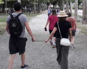 Una persona non vedente e la sua guida, che la segue con cordicella, praticano Fitwalking al Parco Ruffini, visti di spalle